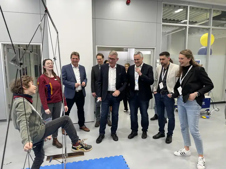 Group of people observing a child using a suspended swing or balance apparatus indoors.