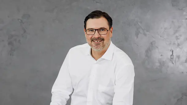 Man in a white dress shirt against a gray textured background.