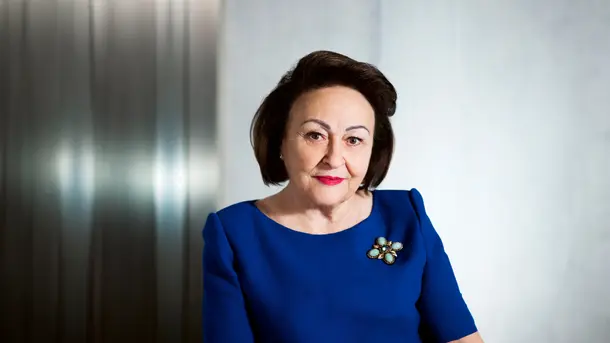 Woman in a royal blue dress with a jeweled brooch on the left shoulder.
