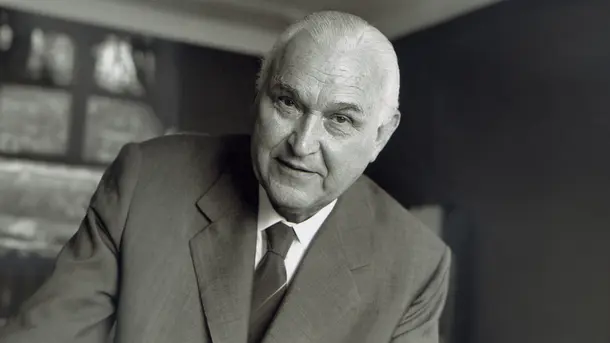 Older man in a suit and tie leaning forward.