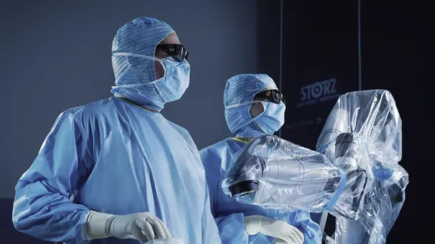 Surgeons wearing surgical masks and gowns operate a robotic surgery system.