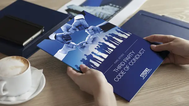 Person holding a booklet titled Third Party Code of Conduct with business-themed graphics on the cover.