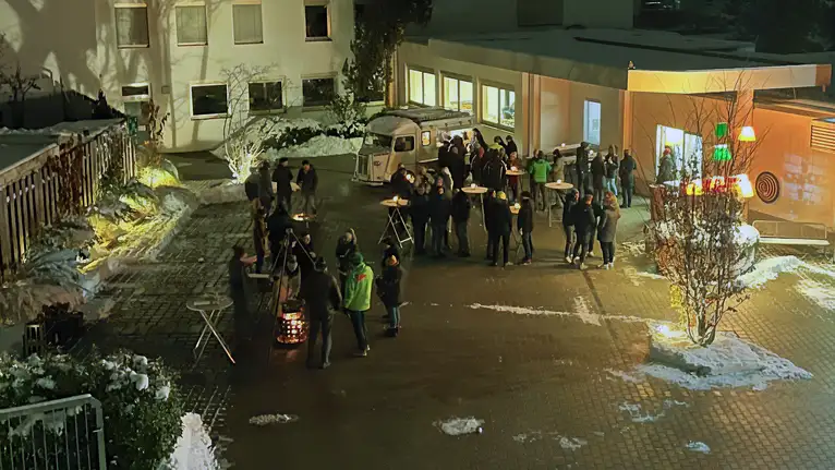 Menschen stehen bei einer Outdoor-Veranstaltung im Winter an Stehtischen und einem Foodtruck.