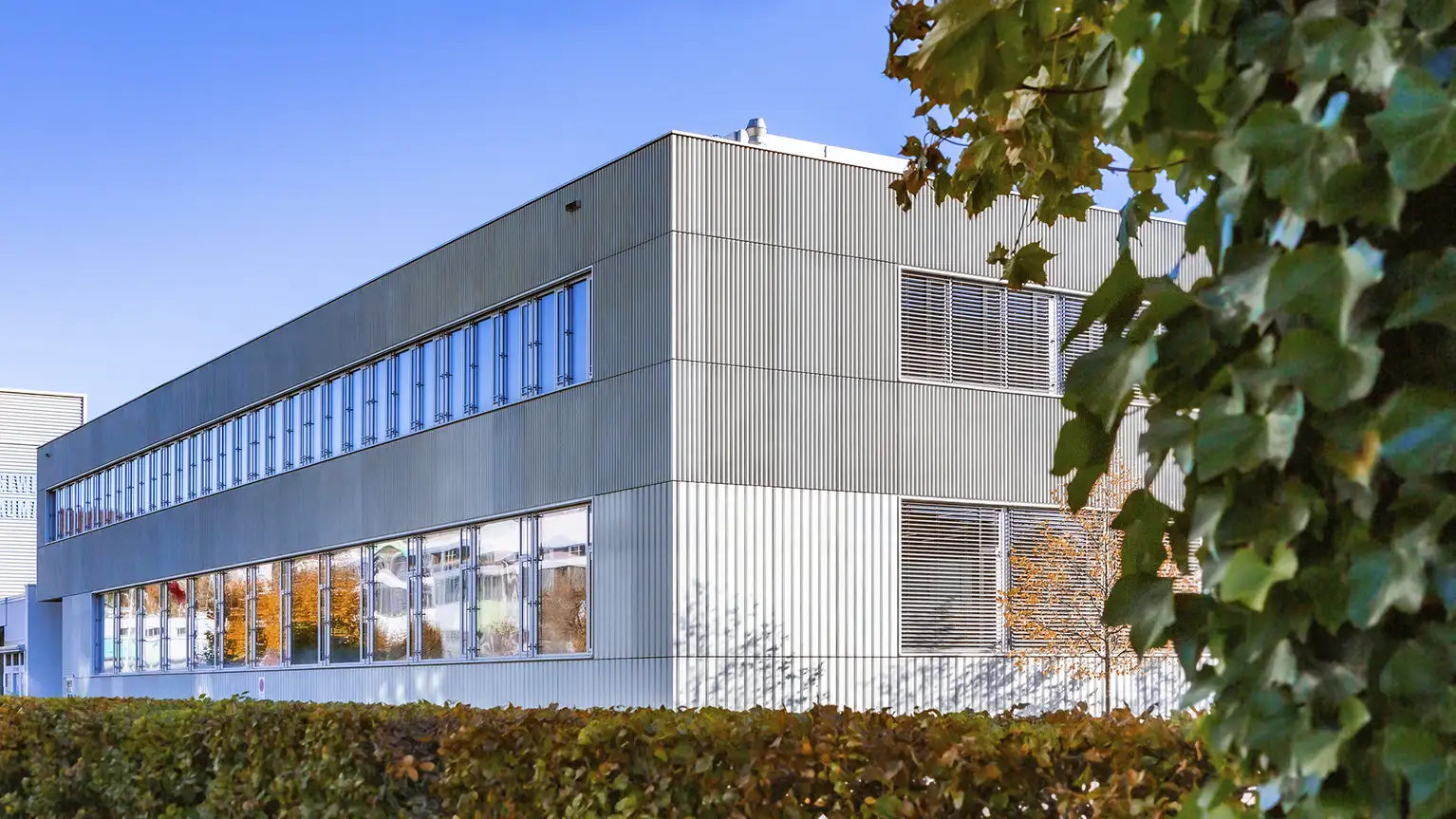 Modern industrial building with large windows and metallic façade under clear blue sky.