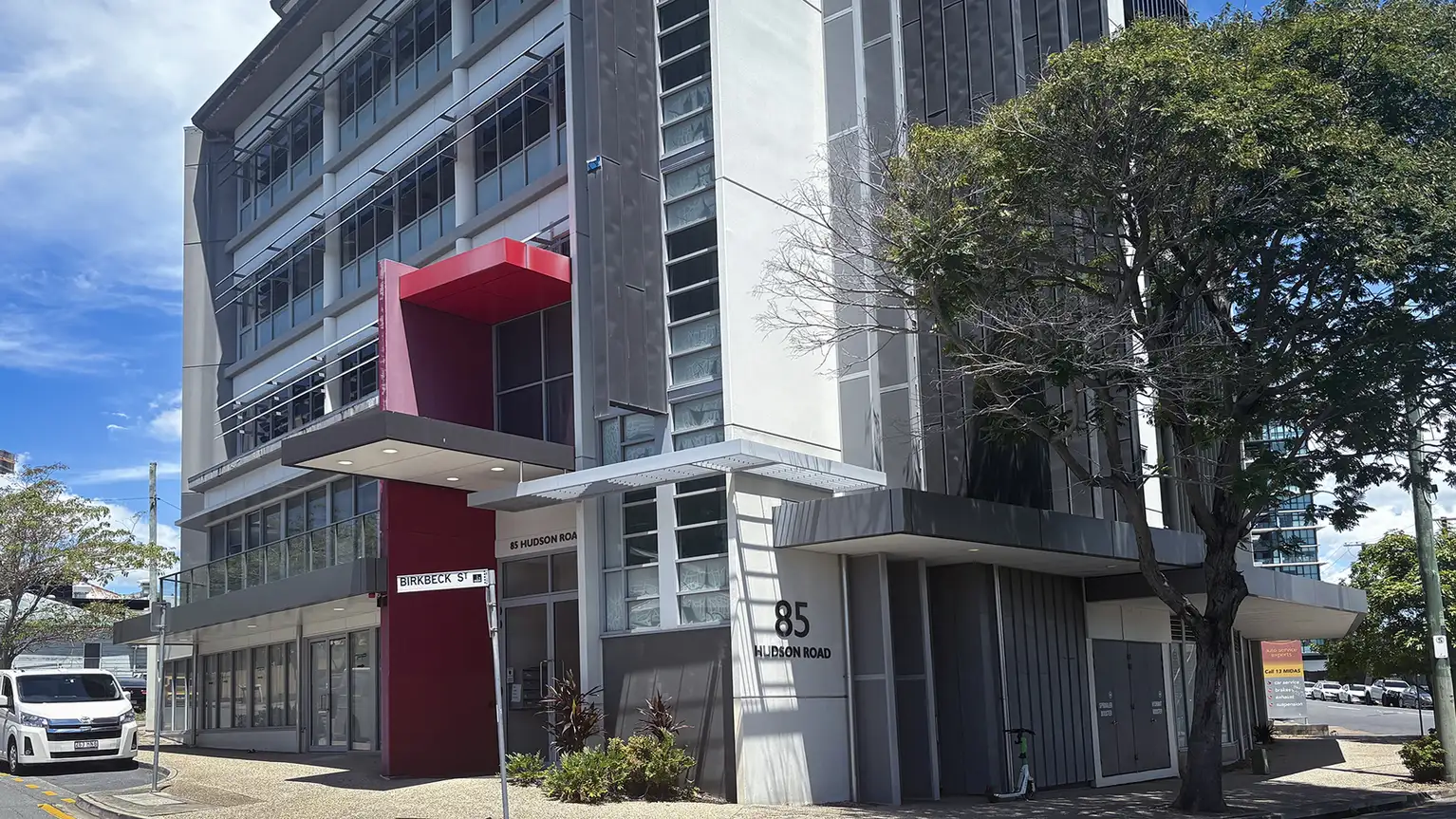 Edificio moderno de oficinas en la esquina de Hudson Road y Birkbeck Street con fachada de vidrio y paneles.