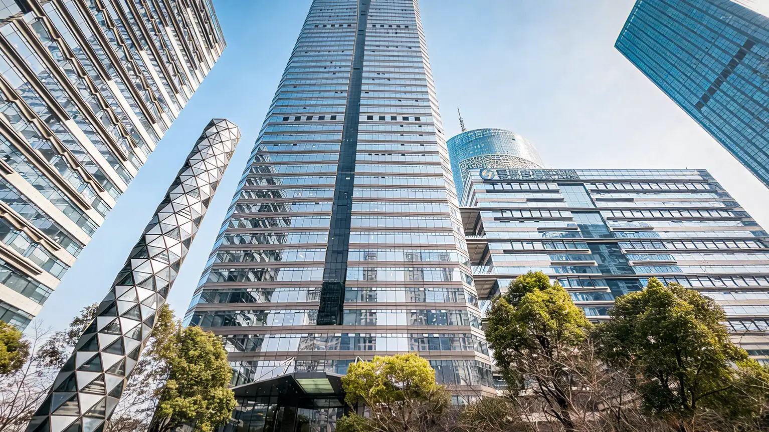 Rascacielos modernos de cristal reflejando el cielo azul en una zona financiera con árboles en primer plano.
