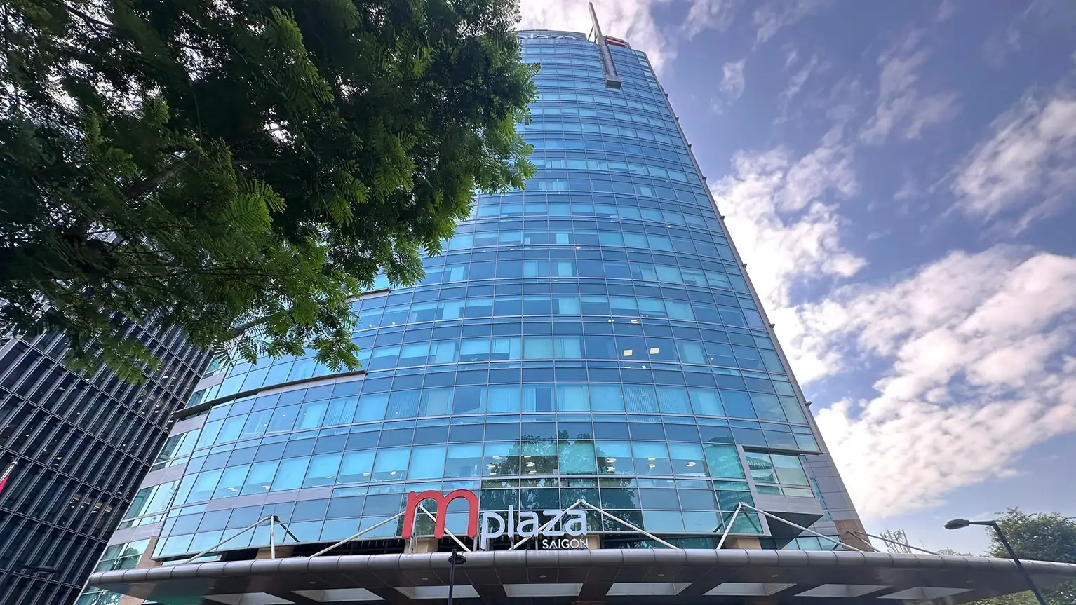 Современное офисное здание из стекла с вывеской m plaza Saigon у главного входа.