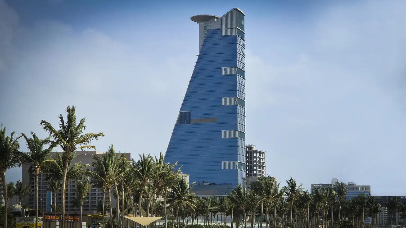 Edificio moderno en forma triangular azul rodeado de palmeras en una ciudad tropical.