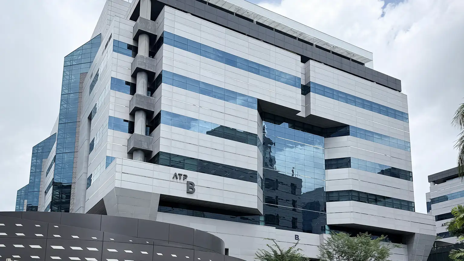 Edificio moderno de oficinas con ventanales de cristal azul reflejando el cielo nublado.
