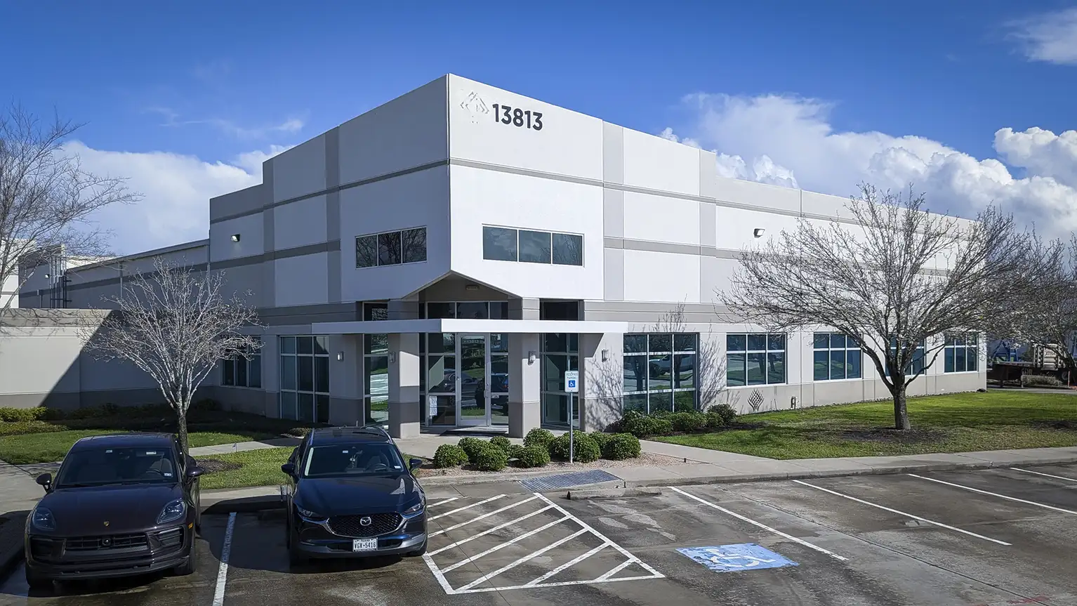 Modern office building with large glass windows and two parked cars in front.