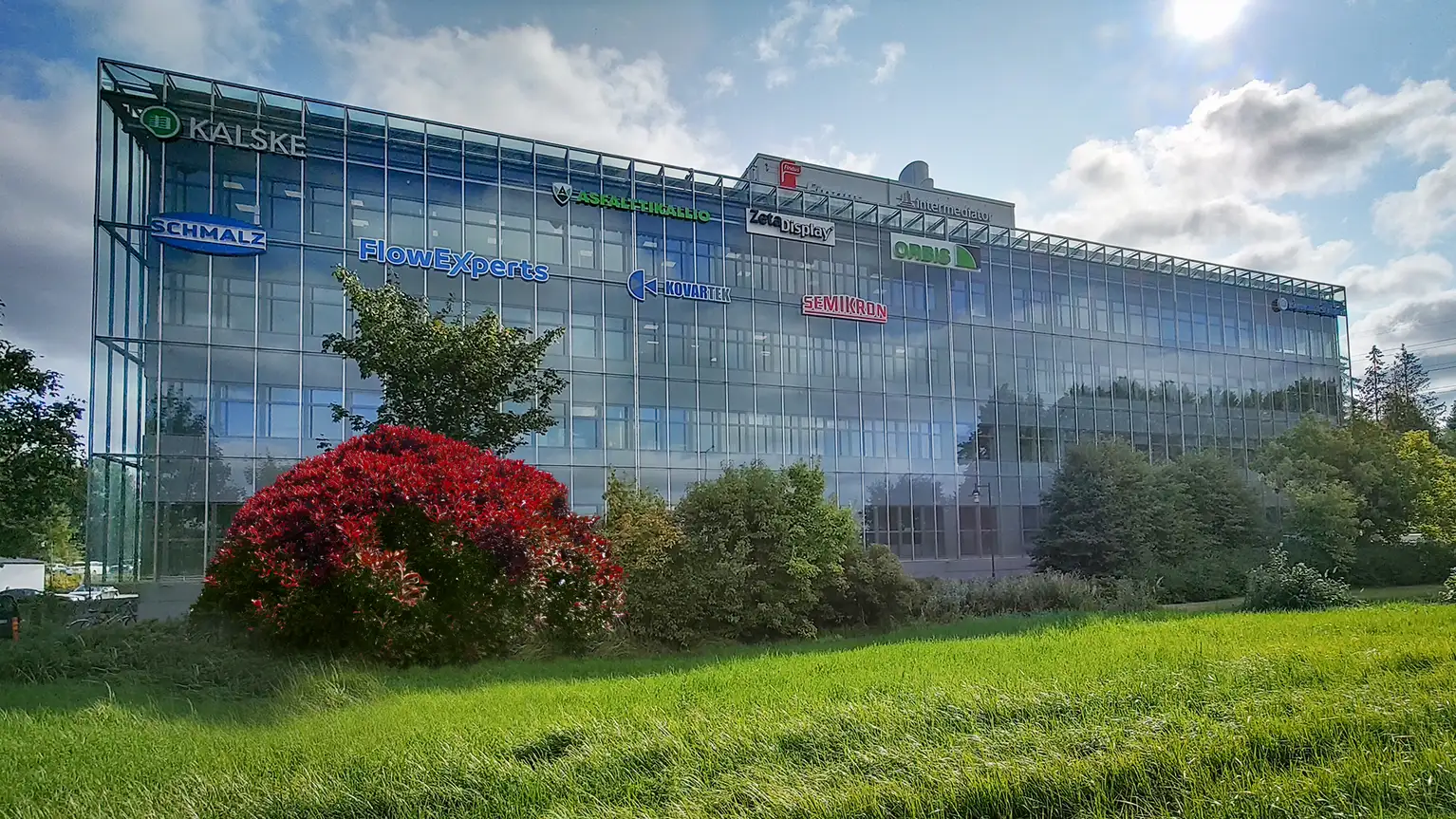 Modern glass office building with company logos on the facade.