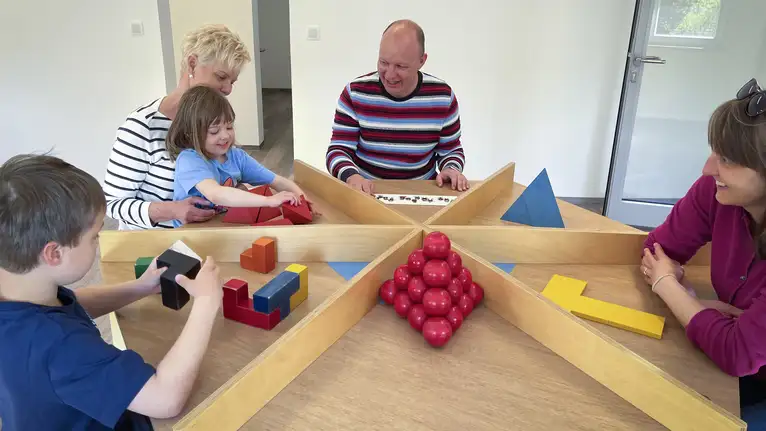 Kinder und Erwachsene spielen gemeinsam mit bunten Holzbausteinen an einem Holztisch.