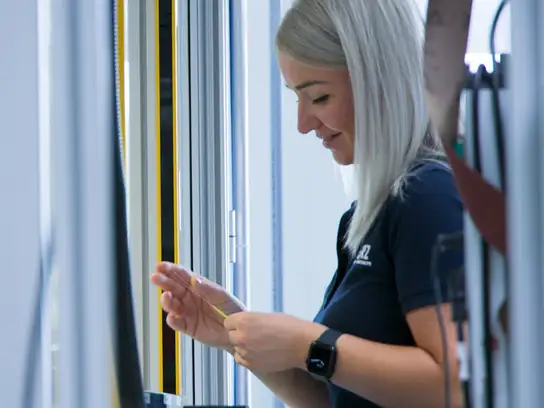 Frau prüft ein technisches Bauteil an einer Maschine.