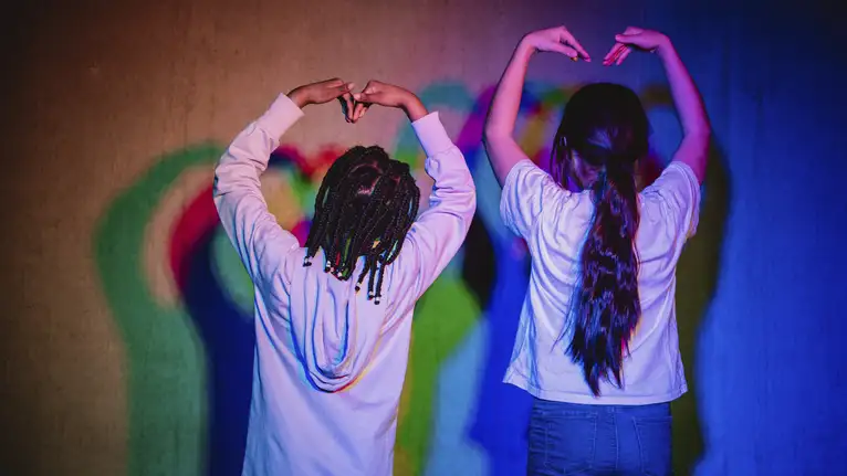 Zwei Kinder mit erhobenen Armen formen Herzen mit den Händen, bunte Lichter reflektieren auf ihre Kleidung.