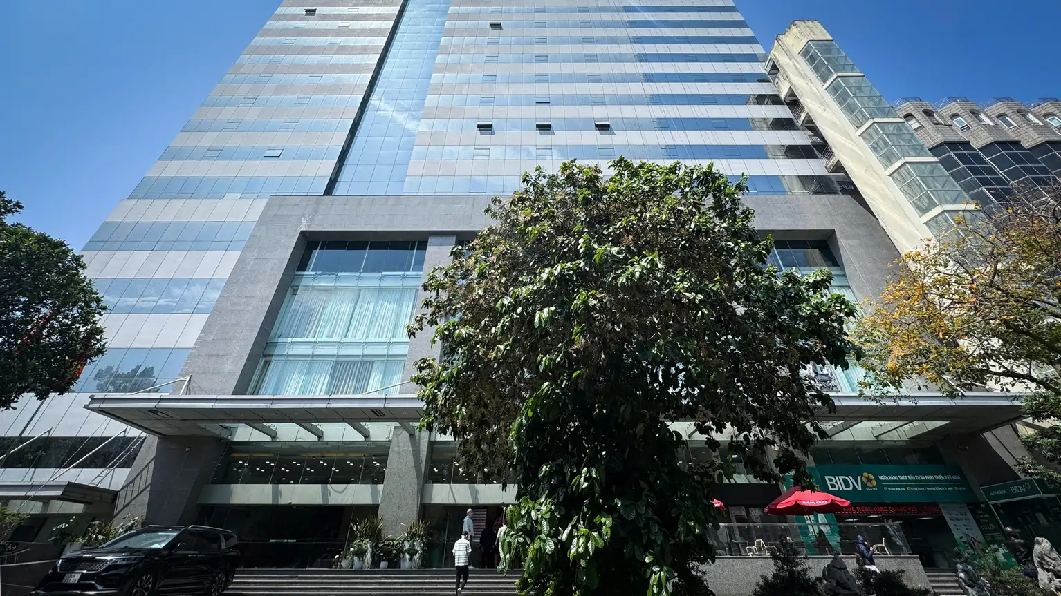 Edificio moderno de oficinas con fachada de vidrio y árboles en la entrada principal.