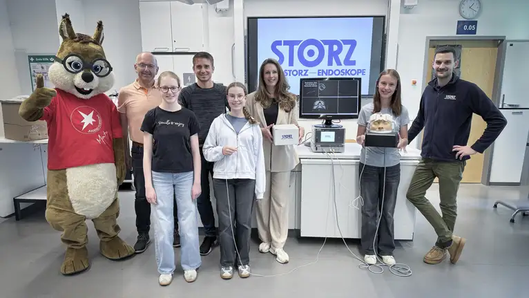 Gruppe von Menschen mit Maskottchen präsentiert medizinische Geräte in einem Labor.