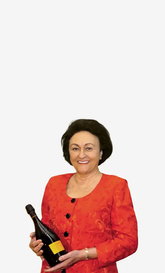 Smiling woman in a red jacket holding a bottle of sparkling wine.
