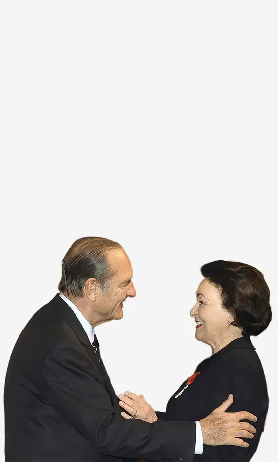 Two elderly people in formal attire smiling and greeting each other.