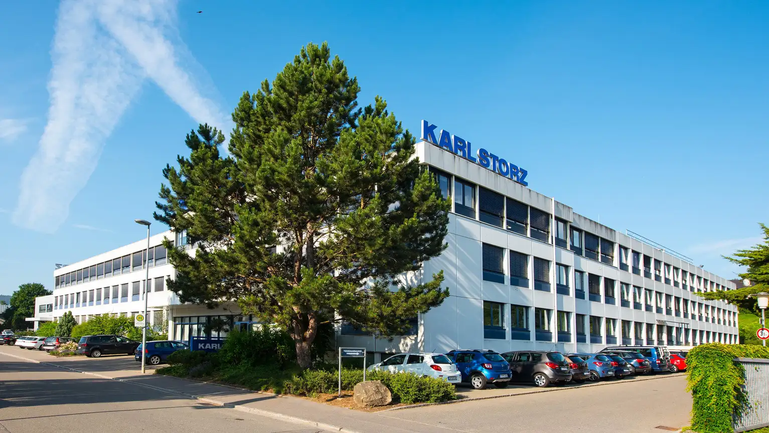 Edificio de oficinas Karl Storz con fachada blanca, árboles y autos estacionados en un día soleado.