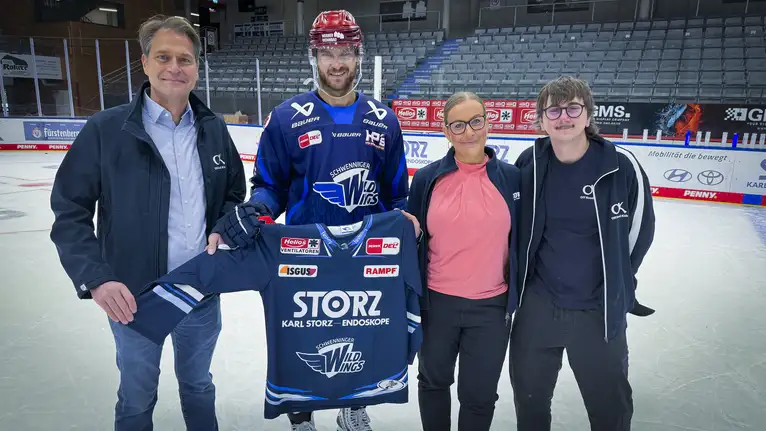 Eishockeyspieler hält gemeinsam mit drei Personen ein Wild Wings Trikot auf dem Eis.