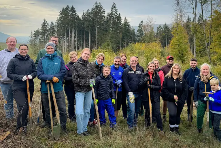 Group of people holding shovels, smiling while participating in a tree planting activity.