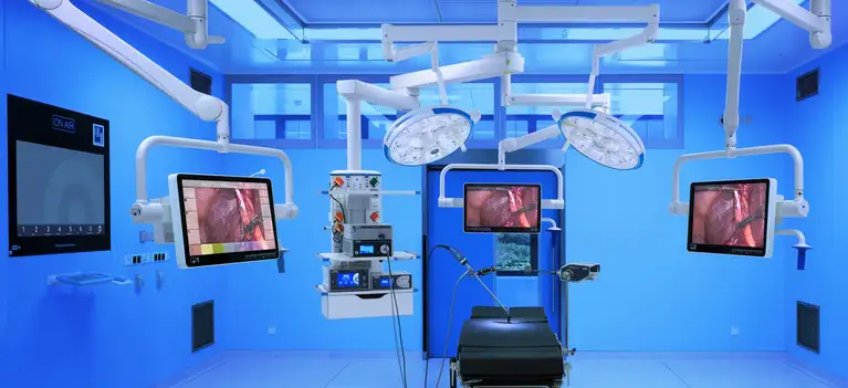 Modern operating room with surgical equipment, monitors displaying endoscopic images, and bright surgical lights.