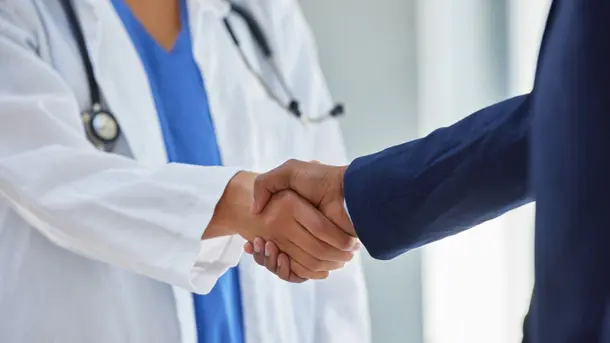 Doctor in white coat shaking hands with a businessperson.