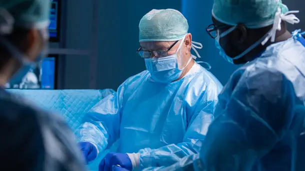 Surgeons in blue sterile gowns and gloves perform a medical procedure in an operating room.