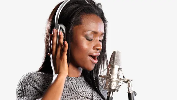Woman wearing headphones and singing into a studio microphone.