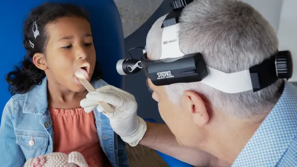Doctor examines a young child's throat using a headlamp and gloves.