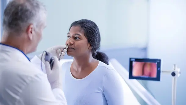 A doctor performs a throat endoscopy on a patient using a flexible scope, with results displayed on a monitor.