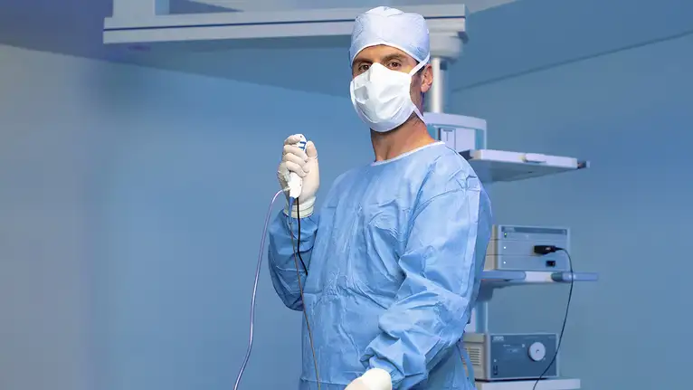 Surgeon in blue scrubs holding a medical instrument in an operating room.