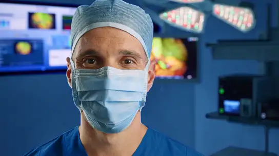 Surgeon wearing a blue surgical cap and gown standing in an operating room.