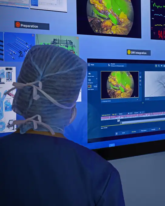 Surgeon in scrubs viewing digital endoscopy images on a large medical monitor in an operating room.