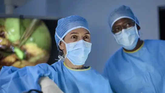 Surgical team wearing blue gowns and masks performing a medical procedure.