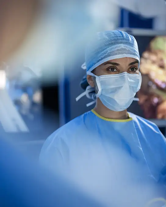 Surgeon wearing blue surgical gown, mask, and cap in an operating room.