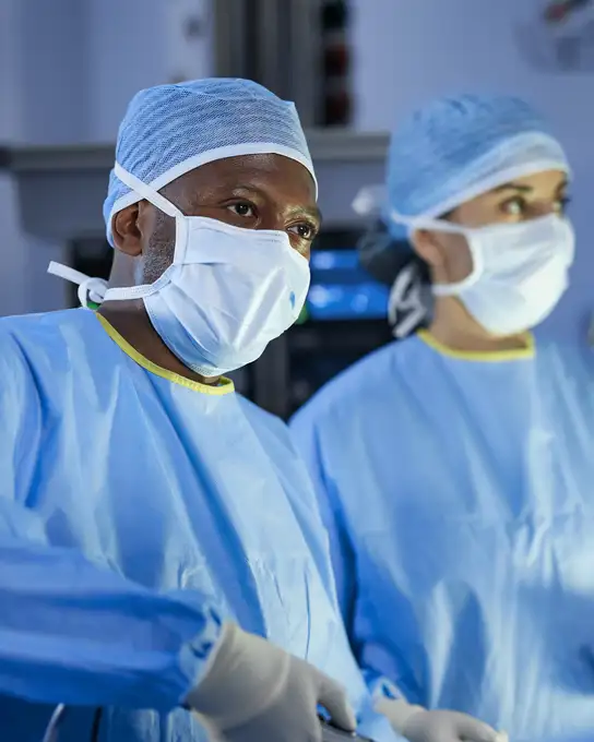 Two surgeons in blue scrubs and masks performing a medical procedure.