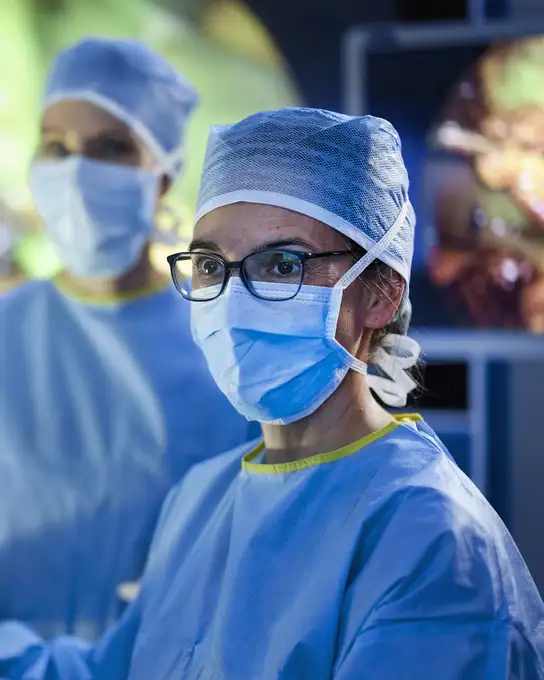 Surgeons wearing blue surgical attire and caps performing an operation in an operating room.