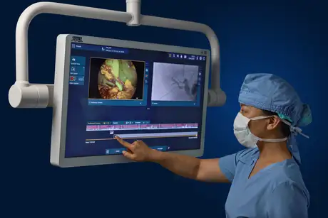 Medical professional in scrubs using a touchscreen to review endoscopic images on a large medical monitor.