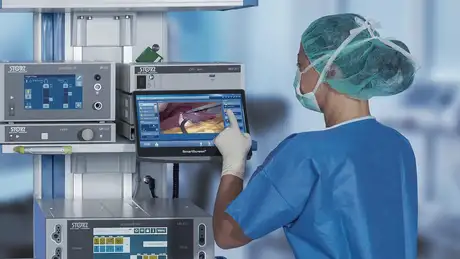 A medical professional operates a touchscreen monitor displaying a laparoscopic surgery procedure.