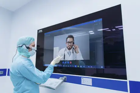 Medical professional in scrubs using a touchscreen for a video consultation with a doctor.