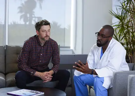 Doctor in white coat discussing results with a patient using a tablet during a consultation.