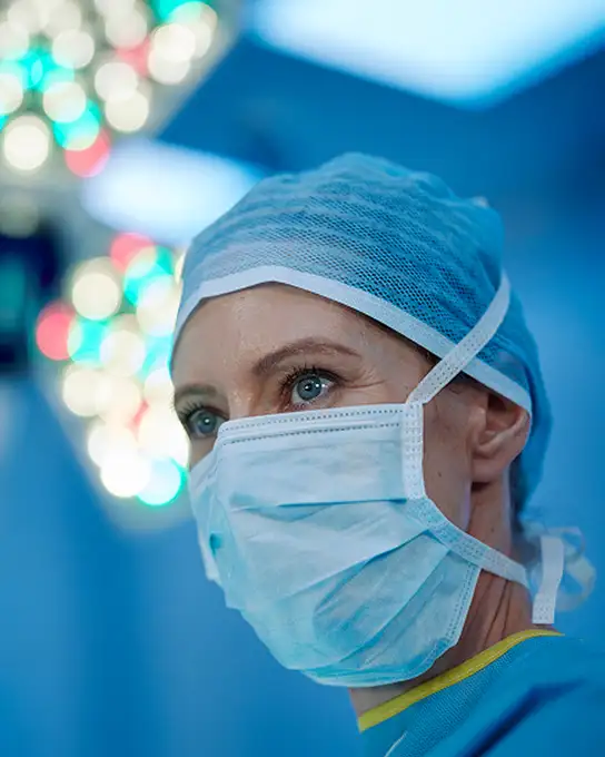 Surgeon wearing a surgical mask, cap, and gown in an operating room.