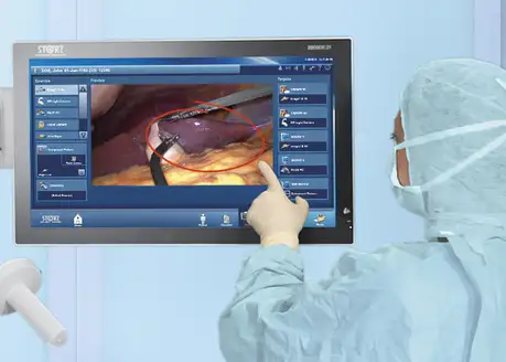 Gloved hand interacting with a medical touchscreen displaying a surgical procedure image.
