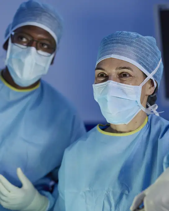 Surgeons wearing blue surgical gowns, gloves, and caps in an operating room.
