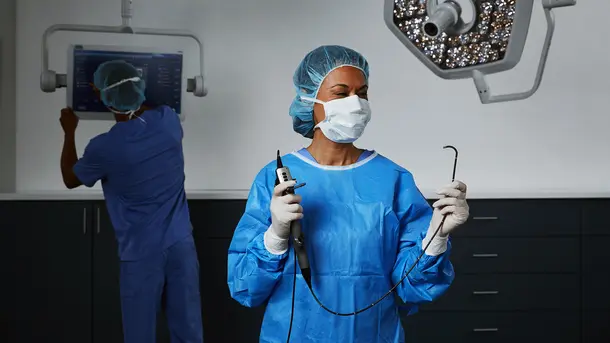 Surgeon in blue scrubs holding medical instruments in an operating room.