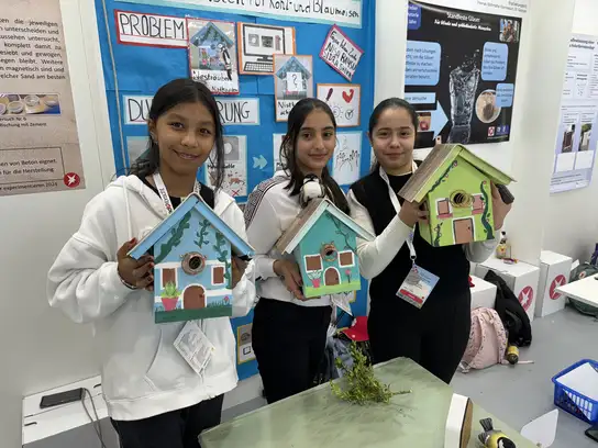 Drei Personen halten selbst bemalte Nistkästen aus Holz in den Händen.