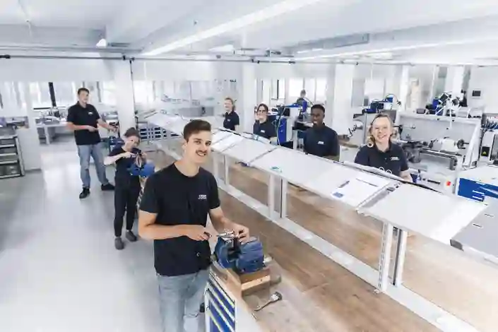 Young trainees working with metal vices and tools at workstations in a technical training workshop.