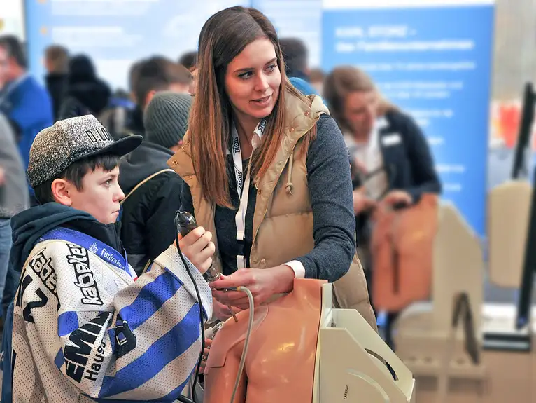 Frau und Kind bedienen gemeinsam ein Gerät auf einer Messe oder Veranstaltung.