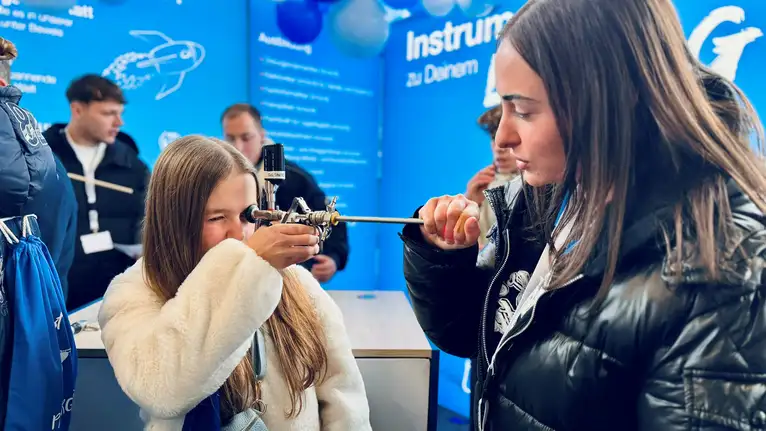 Person hält ein medizinisches Instrument und demonstriert dessen Anwendung an einer anderen Person.